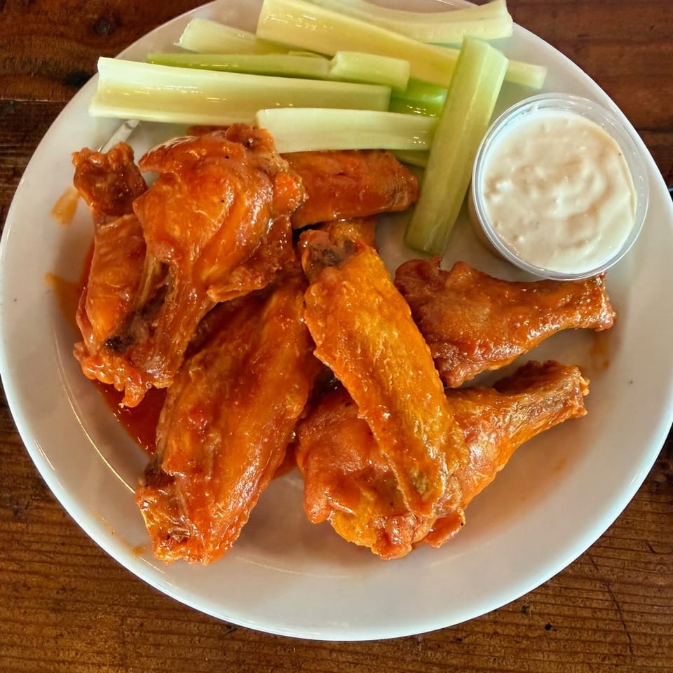 Buffalo chicken wings with celery sticks and creamy dipping sauce on a white plate atop a wooden table.