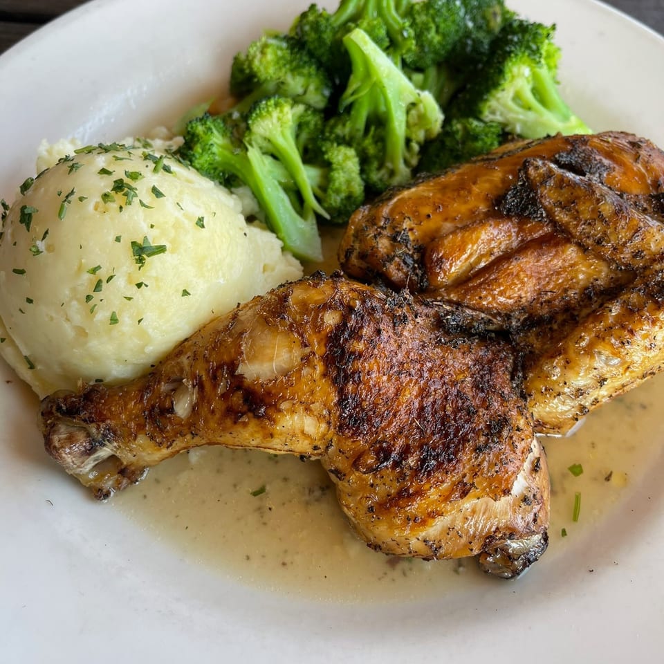 Roasted chicken thighs served with mashed potatoes and steamed broccoli on a white plate.
