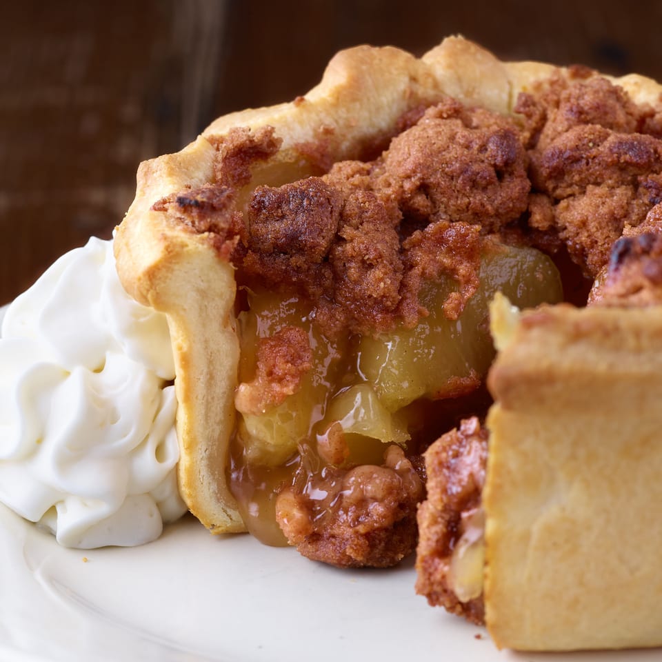 Close-up of a golden pastry filled with fried chicken, green peppers, and sauce, served with whipped cream on a plate.