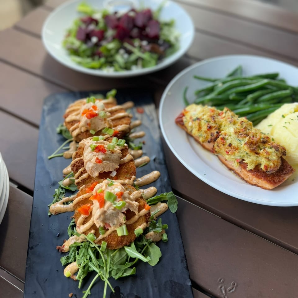 Assorted restaurant dishes include breaded cutlets with creamy sauce, roasted salmon with green beans and mashed potatoes, and salad.